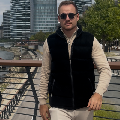 Man wearing sunglasses and a black vest standing in front of modern buildings